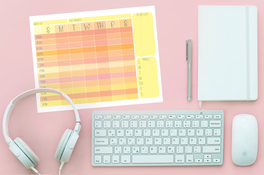 Pink background with a print out of the digital planner in sunrise palette, along with white headphones, white keyboard, white notebook, and a mouse